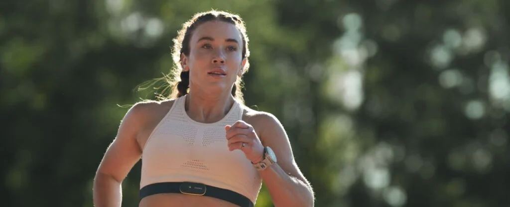 Pelari wanita mengenakan smartwatch Garmin dan heart rate monitor (chest strap) saat latihan lari outdoor.