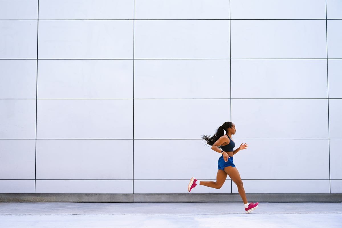 Seorang wanita yang mengenakan smartwatch Garmin Forerunner 970 sedang berlari di depan sebuah gedung.