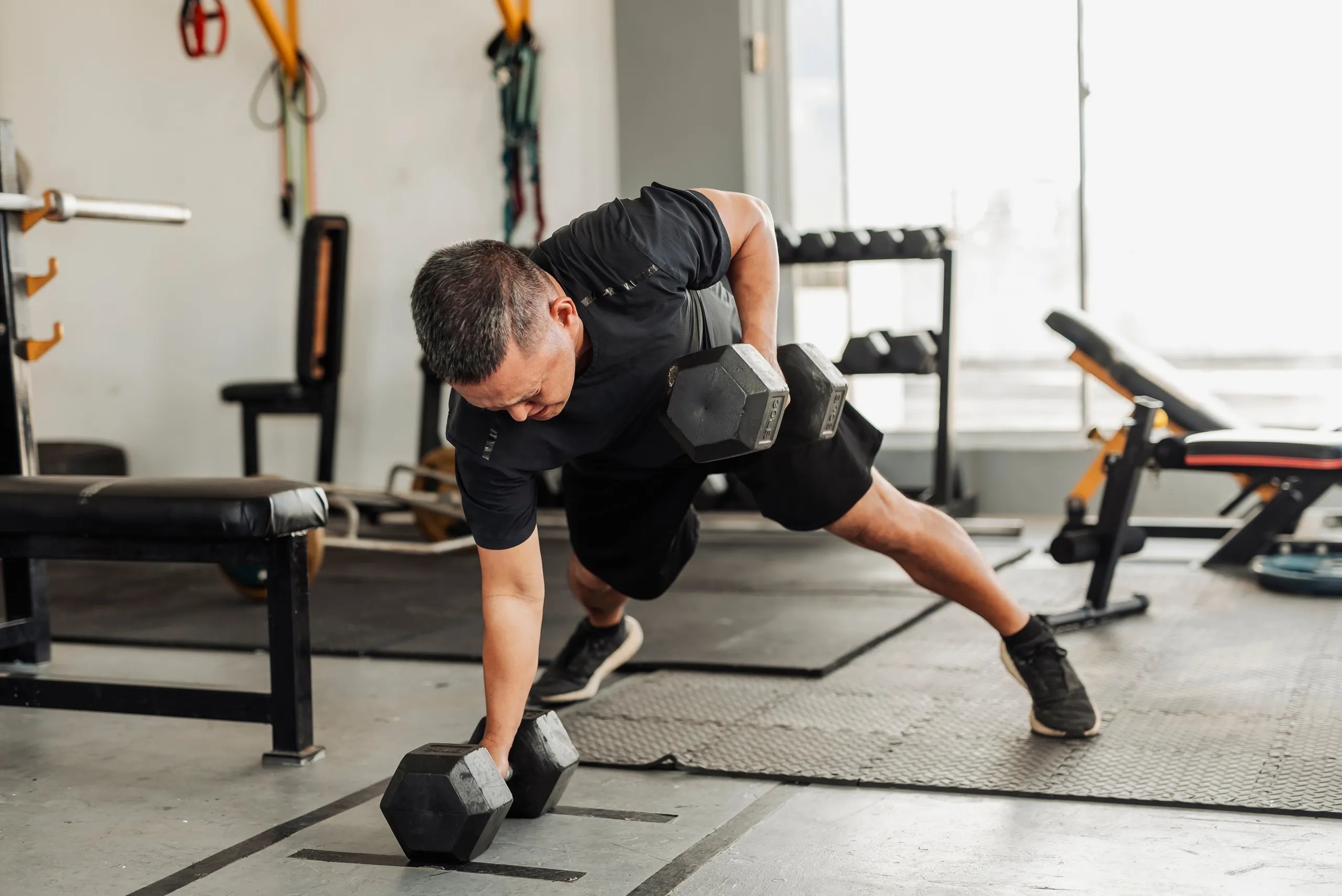 Latihan Kekuatan dengan Dumbbell: Pria Melakukan Gerakan Renegade Row di Gym